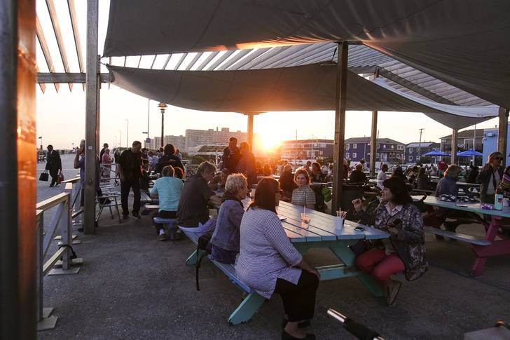 A crowd of folks gather over dinner at sunset on the Rockaway Boardwalk in Queens.